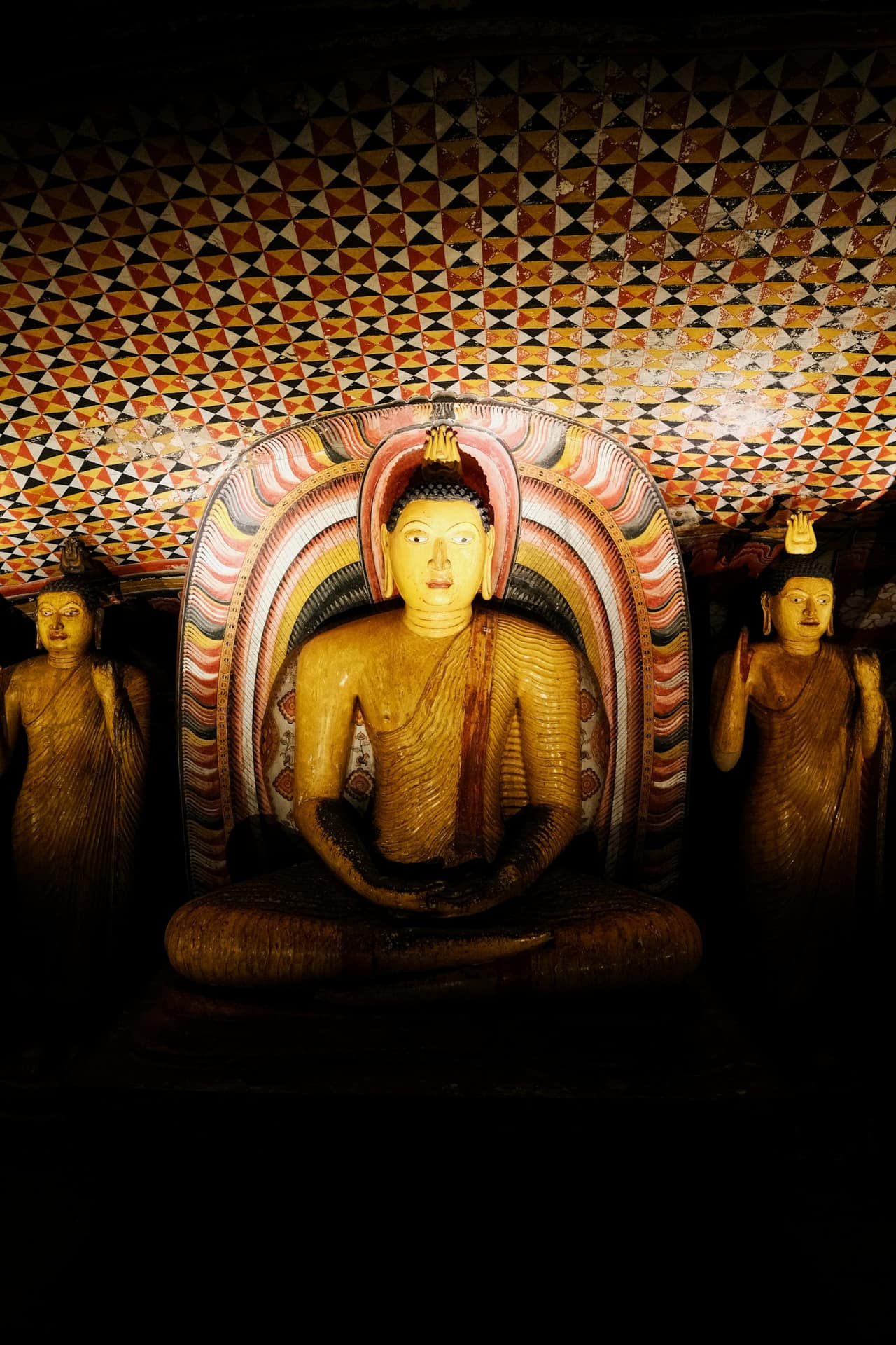 Rows of seated Buddha statues beneath a painted rock ceiling inside the Dambulla cave temple complex